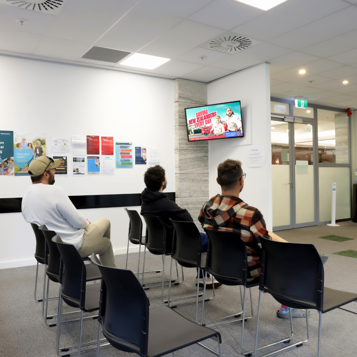 Patients in a medical centre waiting room with a Medtalk screen on the wall